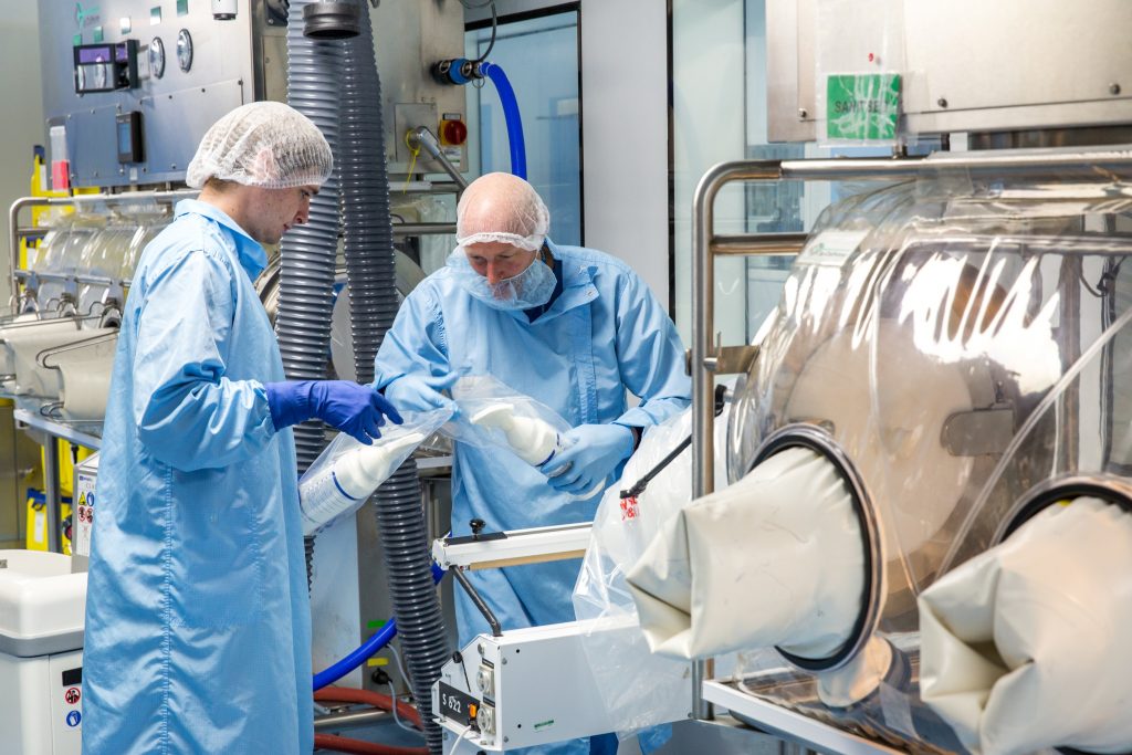 Image shows two male scientists wearing protective clothing in a production zone.