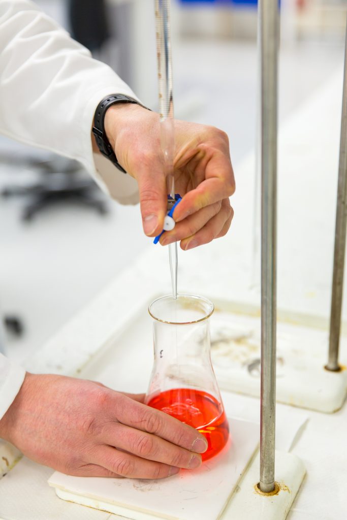 Image shows a scientist's hands holding a container with red liquid in it.