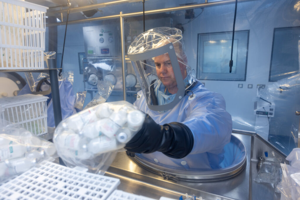 A man in full protective equipment handles containers in a cabinet.