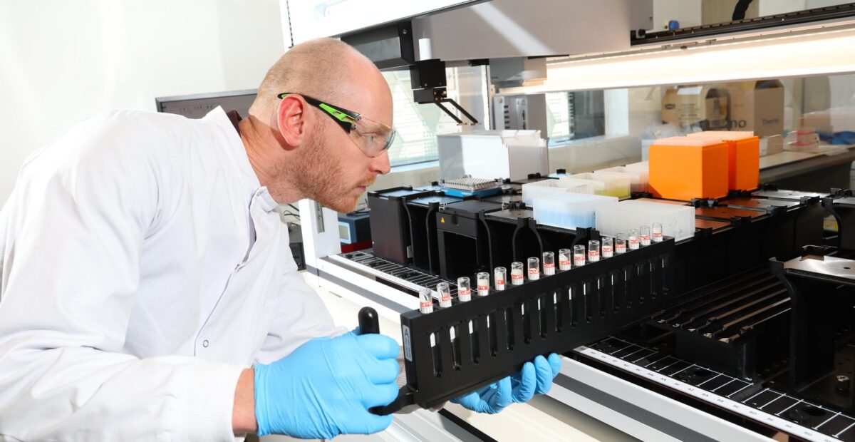A scientist wearing safety glasses handling a rack of test tubes.
