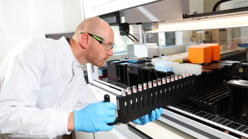 A scientist wearing safety glasses handling a rack of test tubes.
