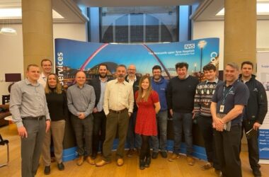 The image shows Charlotte Fox who leads the innovation team with guests in front of a banner stand at an innovation event.