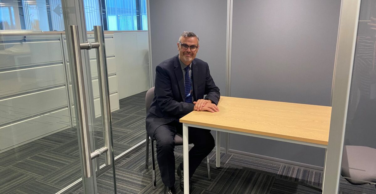 The image shows Chris Speed sitting at a table in one of the sound proof glass pods.