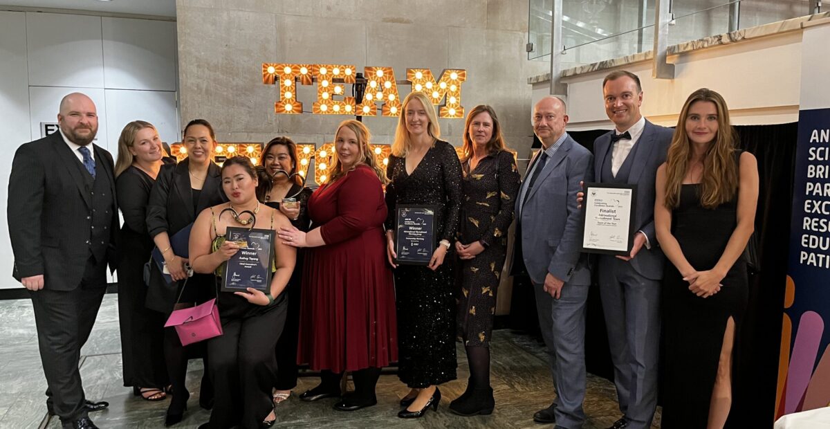 The team together at the awards ceremony. Three people are holding certificates. They are all smiling for a photo.