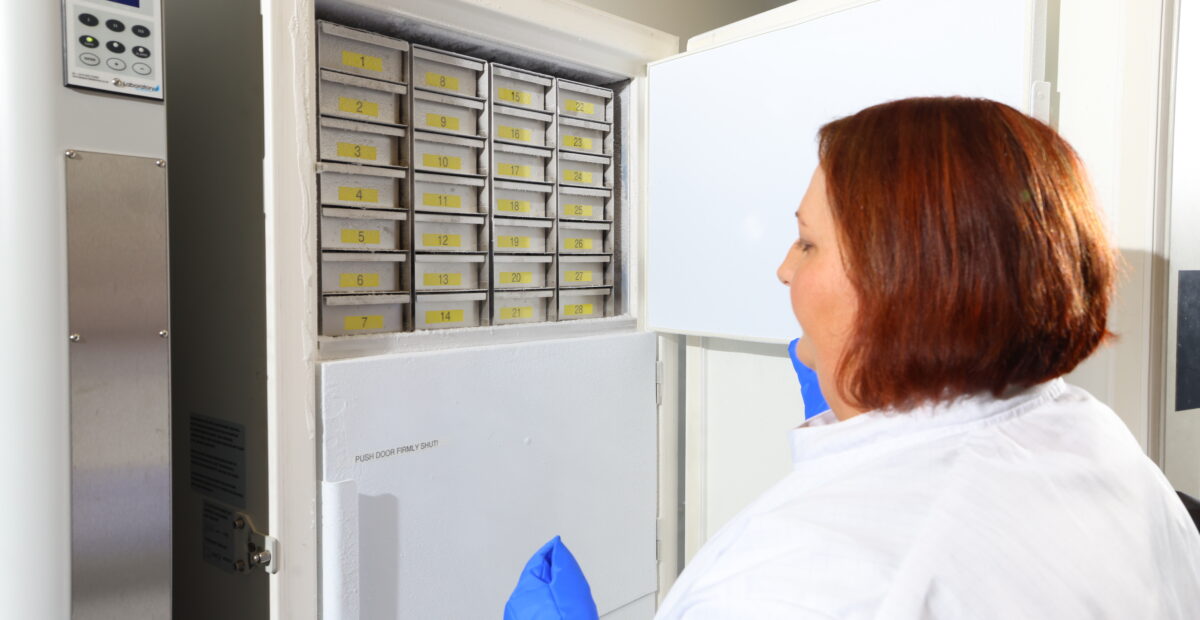 A scientist opening the biobank wearing a white lab coat and blue gloves.