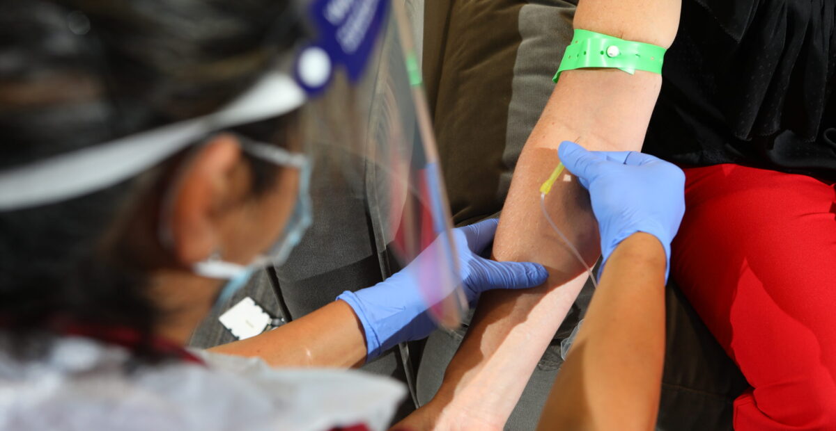 A nurse drawing blood from a patient wearing PPE and a green strap tied around the patients arm.