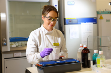 A scientist doing a test wearing a white lab coat and a yellow identification badge.