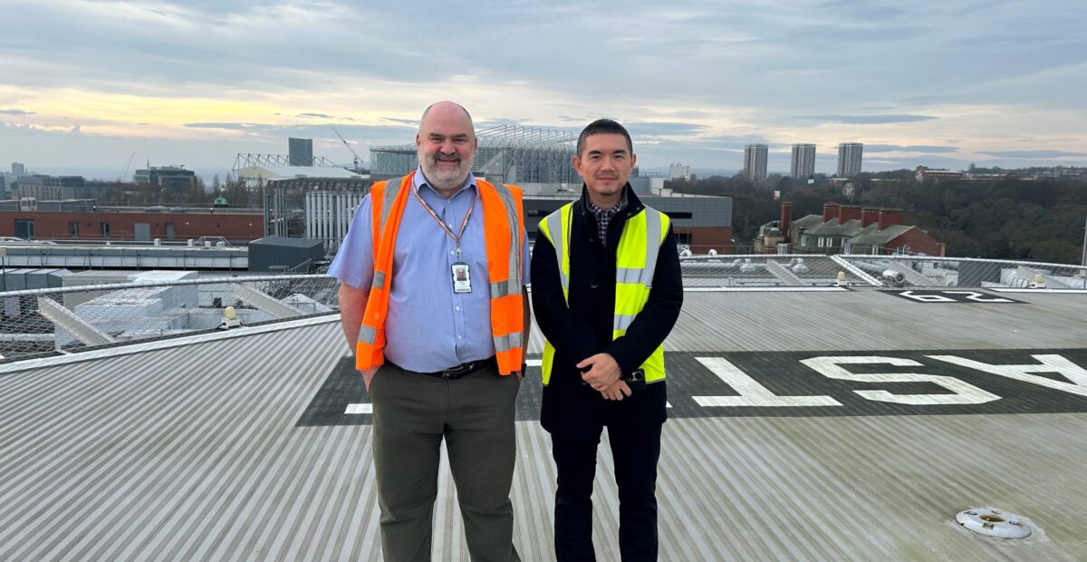 Two men standing on the helipad of the RVI wearing orange and yellow hi-vis clothing.