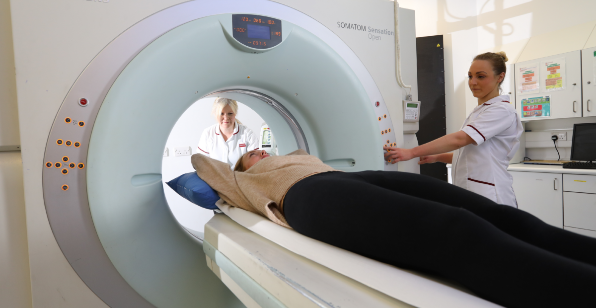 A patient in a scanner with two members of staff who are wearing white uniforms.