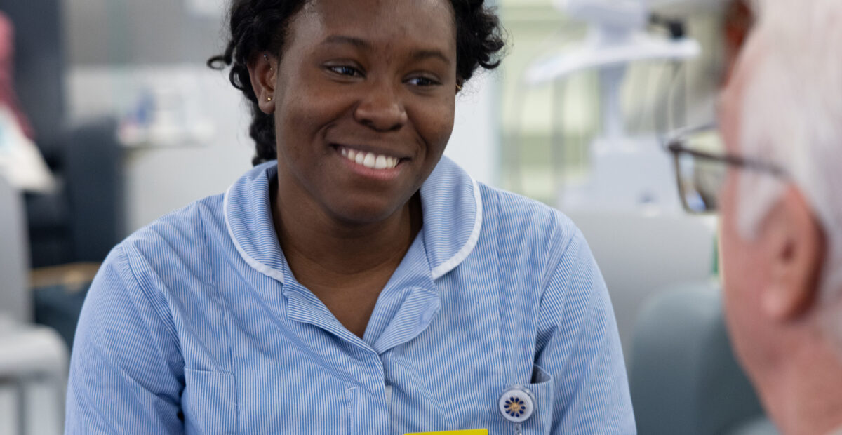 Nurse talking to a patient wearing her uniform and a yellow identification badge.