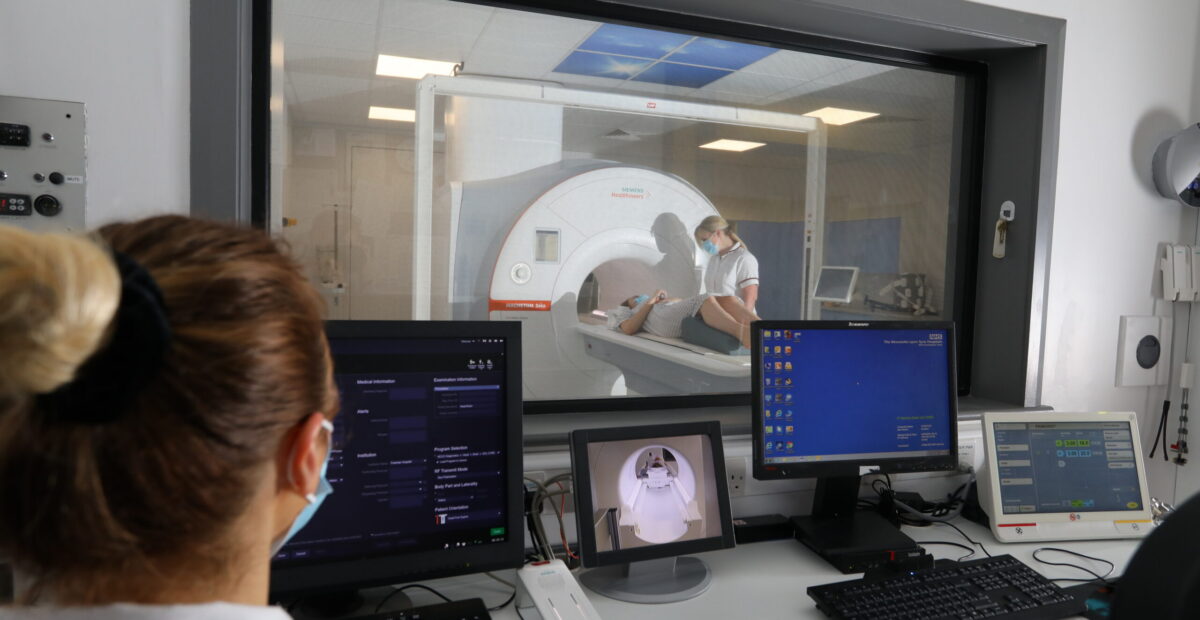 Patient in scanner from a control room with staff wearing blue masks.