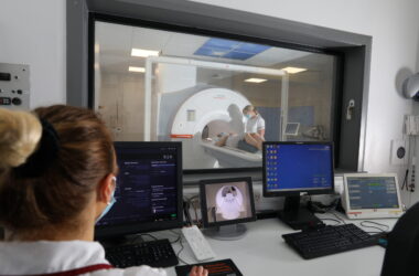 Image shows patient in scanner from a control room with staff wearing blue masks