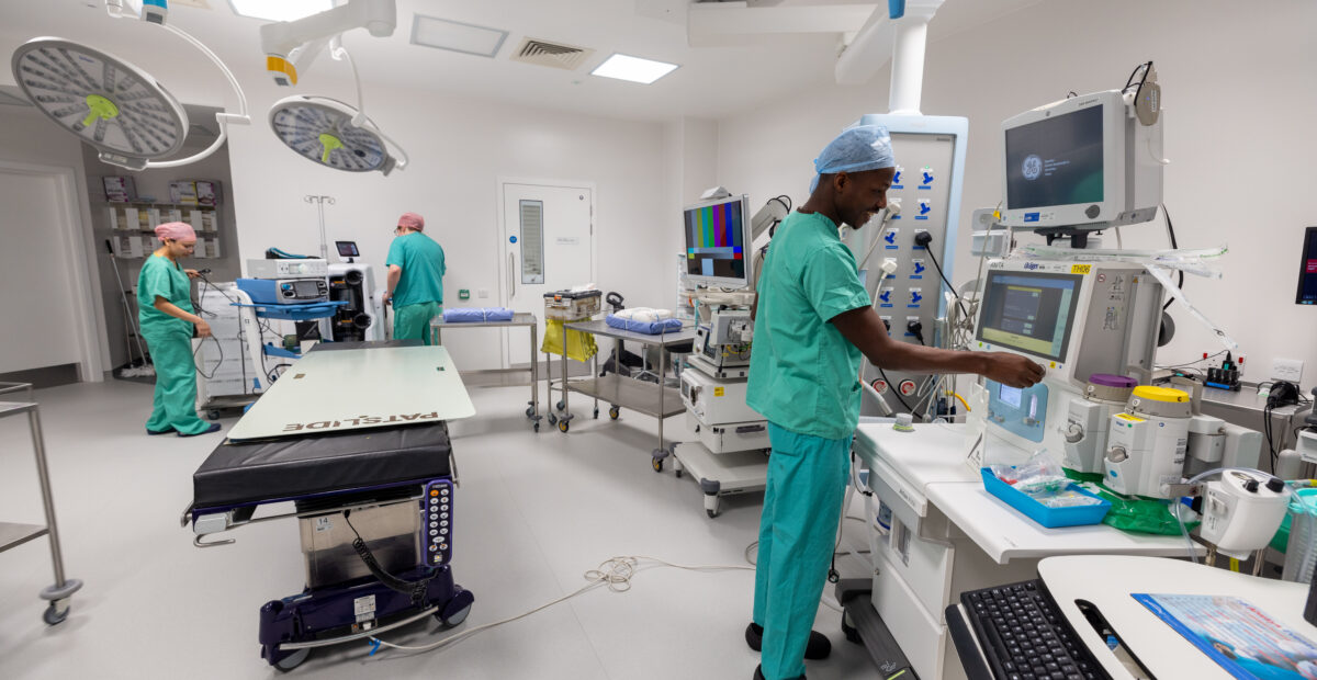 Members of staff in operating theatre, wearing scrubs and PPE, setting up machinery.