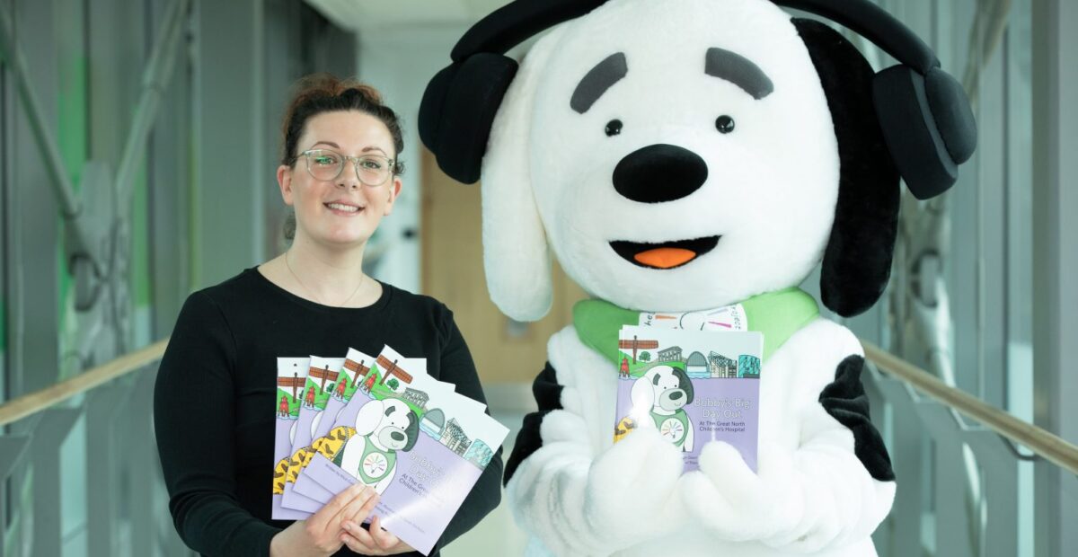 Bobby the mascot with his book, standing next to Alice Gair who is also holding the book.