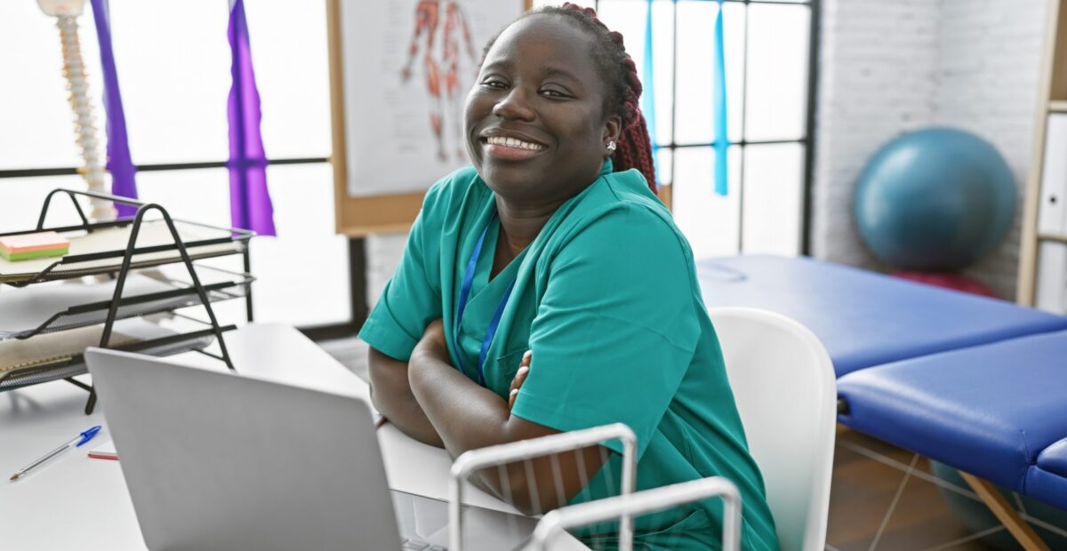 A,Smiling,African,American,Woman,With,Braids,,Wearing,Scrubs,,Sitting