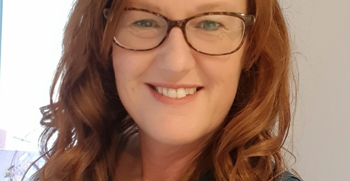 A woman with red hair and glasses smiling.