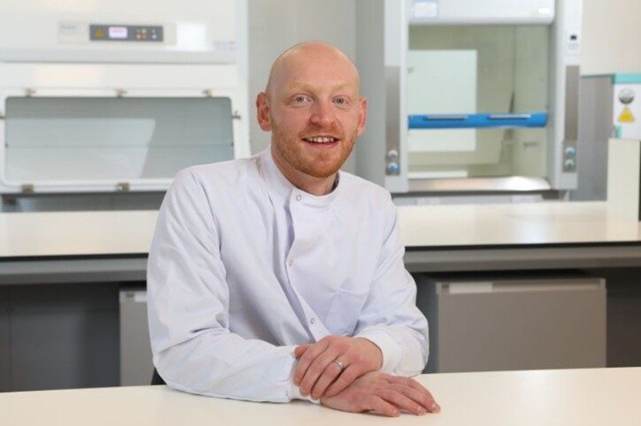 A member of staff wearing a lab coat, sat at a table in the lab.