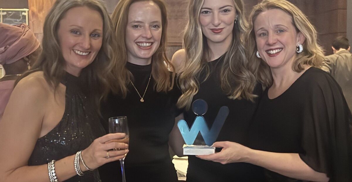 A group of women smiling, wearing black dresses holding an award.