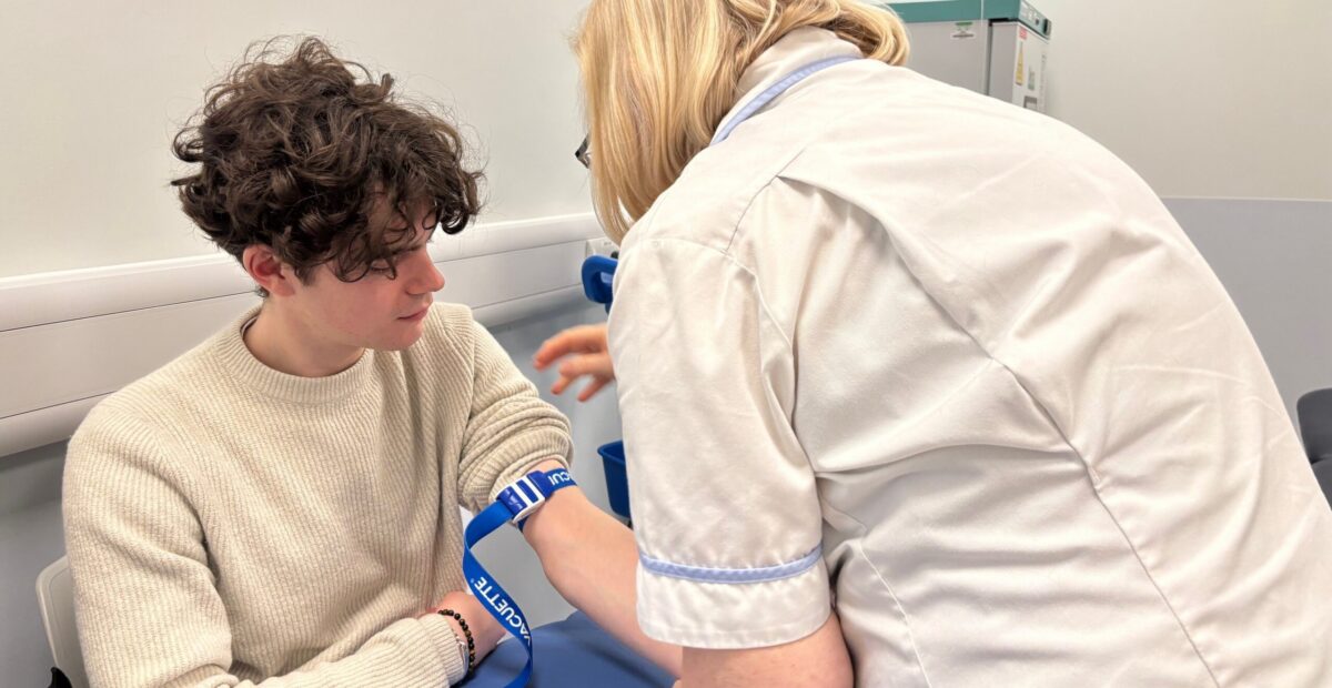 A nurse playing a strap around a patients arm who is sat down. He is about to get bloods taken.