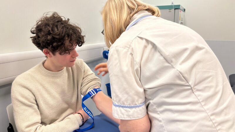 A nurse playing a strap around a patients arm who is sat down. He is about to get bloods taken.