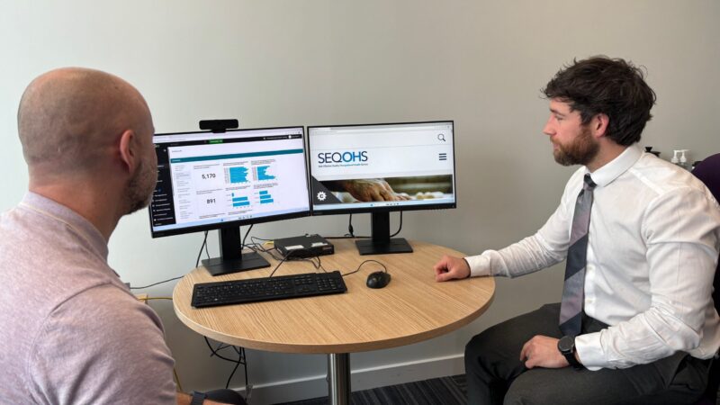 Two men sat at a desk discussing information which is displayed on a computer screen.
