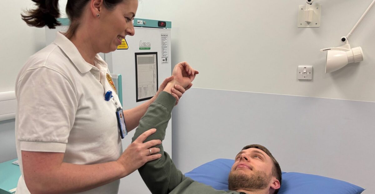 A physiotherapist holding a mans arm up who is lying on a treatment bed.