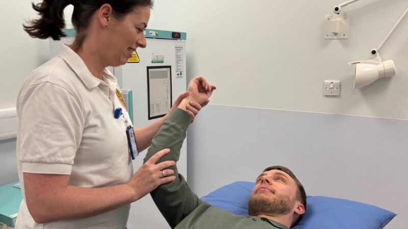 A physiotherapist holding a mans arm up who is lying on a treatment bed.