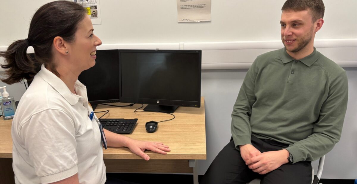A physiotherapist having a conversation with a patient while sat at a desk.