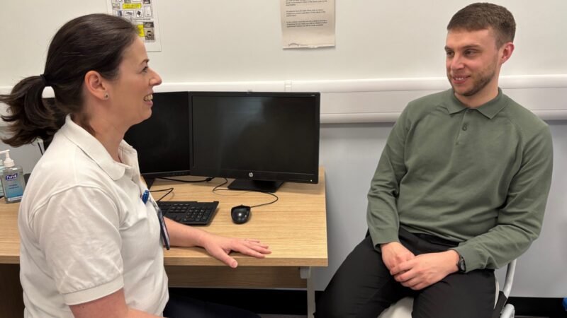 A physiotherapist having a conversation with a patient while sat at a desk.
