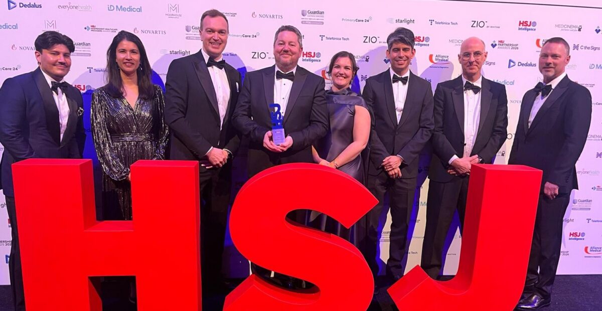 The Newcastle Hospitals and Solventum team standing with their HSJ award at the event, standing behind big HSJ letters in red.