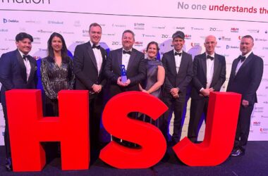 The Newcastle Hospitals and Solventum team standing with their HSJ award at the event, standing behind big HSJ letters in red.