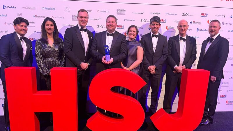The Newcastle Hospitals and Solventum team standing with their HSJ award at the event, standing behind big HSJ letters in red.