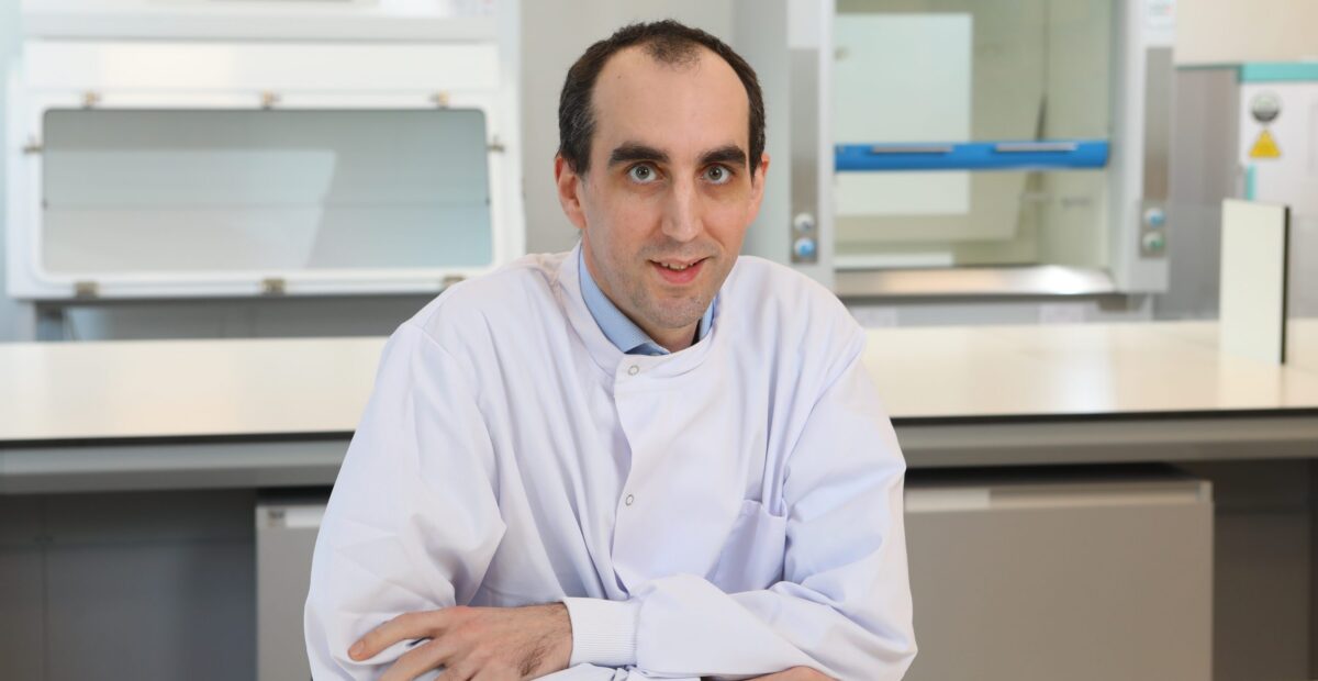Dr John Tyson in the laboratory, smiling, wearing a white lab coat.