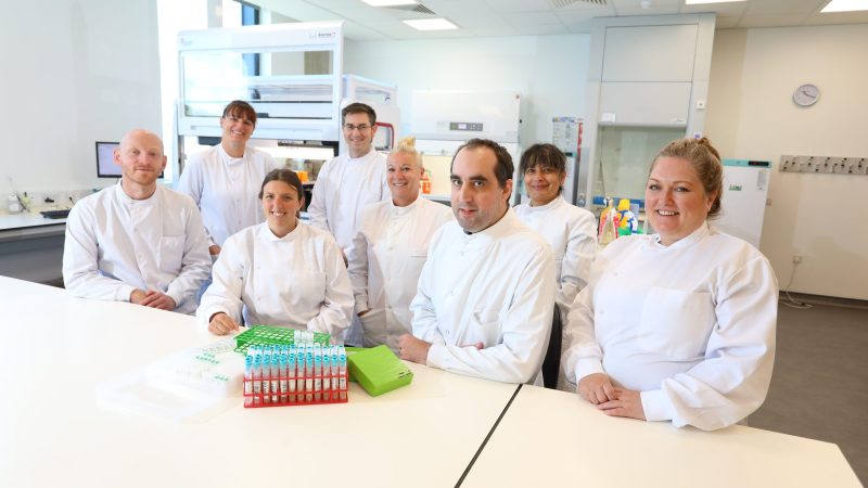 The image shows a picture of the lab team sitting together in the lab smiling.