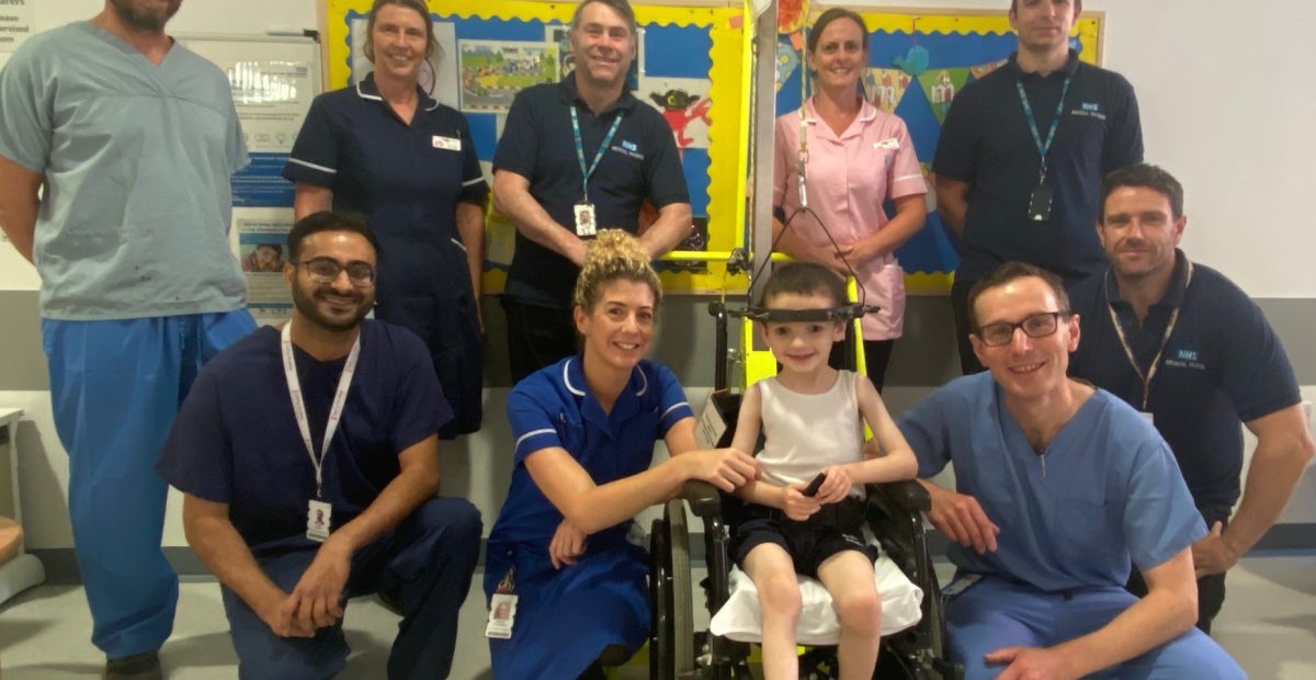 The image shows a group of Newcastle Hospitals staff in hospital with a little boy at the front, wearing a 'halo' device.