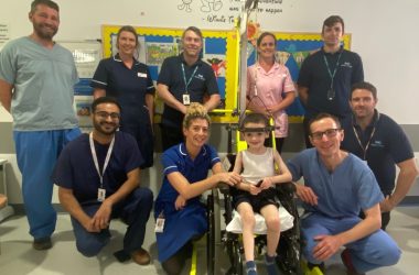 The image shows a group of Newcastle Hospitals staff in hospital with a little boy at the front, wearing a 'halo' device.